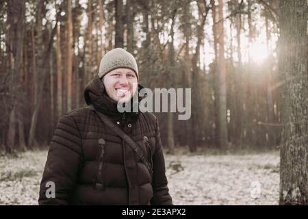 Homme souriant dans la forêt d'hiver. Un homme heureux marche dans la forêt enneigée. Un gars de bonne humeur. Randonnée dans la forêt d'hiver. Voyage en hiver. Nature wal Banque D'Images