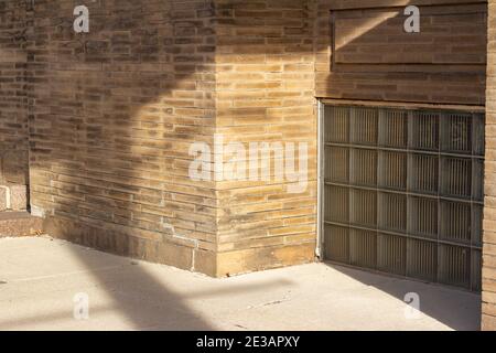 Arrière-plan plein cadre texture d'un mur en brique beige d'extérieur grinçant vintage, avec des fenêtres de sous-sol en bloc de verre uniques, le long d'un trottoir ensoleillé Banque D'Images