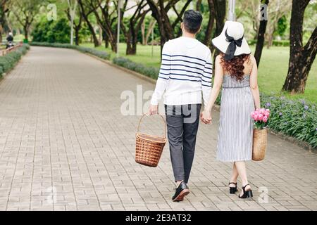 Jeune couple tenant les mains lors de la marche dans le parc de la ville avec paniers à pique-nique Banque D'Images