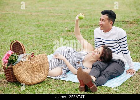 Beau sourire jeune couple asiatique appréciant le picninc dans le parc, manger des fruits et parler Banque D'Images