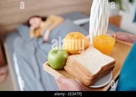 Gros plan de l'homme apportant plateau avec sandwich, jus d'orange et fruits dans le lit où sa femme dormait le matin de la Saint Valentin Banque D'Images