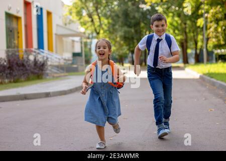 Des écoliers gaies, une fille et un garçon dans une chemise blanche avec des sacs à dos, courent de l'école. Banque D'Images