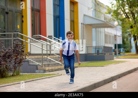 Jeune écolier gai en chemise blanche, cravate bleue et sac à dos court de l'école Banque D'Images