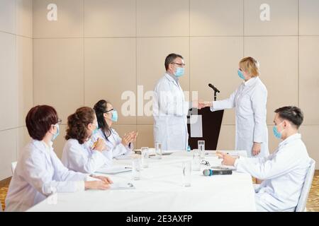 Des chercheurs expérimentés dans les masques médicaux se secouant les mains après avoir réussi conférence médicale dédiée au coronavirus Banque D'Images