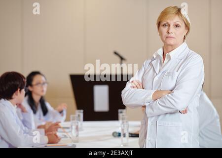 Portrait de chercheuse sérieuse dans les bras pliants de blouse de travail et regarder l'appareil photo Banque D'Images