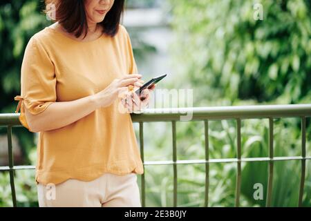Image rognée d'une femme âgée répondant à un message texte sur smartpone ou en vérifiant les notifications dans l'application Banque D'Images