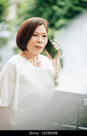Portrait d'une femme asiatique âgée sérieuse parlant au téléphone avec ami ou membre de la famille Banque D'Images