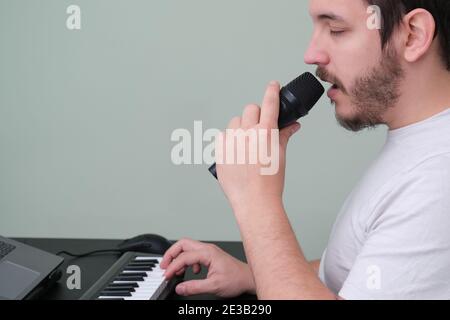 Un homme blogueur, youtuber, influenceur enregistrant une vidéo jouant le piano électronique et chantant à la maison. Musicien, chanteur, pianiste. Banque D'Images