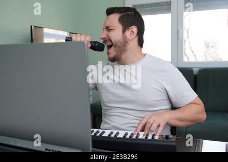 Un homme blogueur, youtuber, influenceur enregistrant une vidéo jouant le piano électronique et chantant à la maison. Musicien, chanteur, pianiste. Banque D'Images