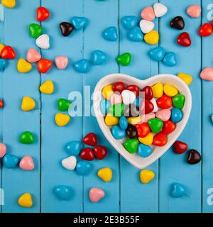 Bonbons multicolores dans une assiette en forme de coeur sur fond bleu en bois. Saint Valentin. Banque D'Images