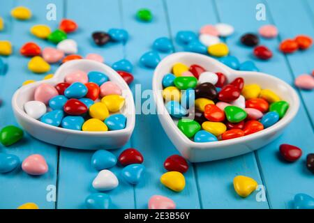 Bonbons multicolores dans une assiette en forme de coeur sur fond bleu en bois. Saint Valentin. Banque D'Images