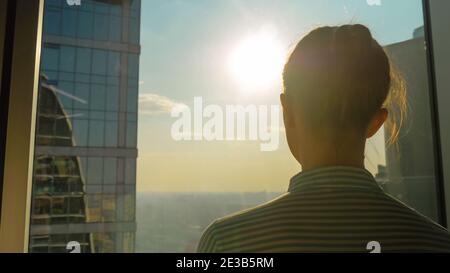 Vue arrière de la silhouette de femme en regardant le paysage urbain par la fenêtre de gratte-ciel Banque D'Images