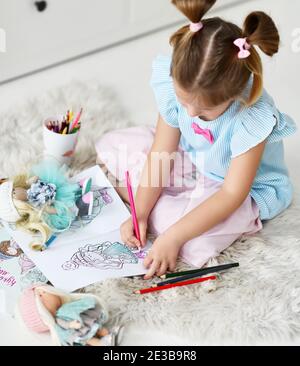 Fille d'enfant avec des petits pains drôles est assis sur le tapis doux à la maison dessin coloriage images de poupées avec des crayons colorés. Vue de dessus Banque D'Images