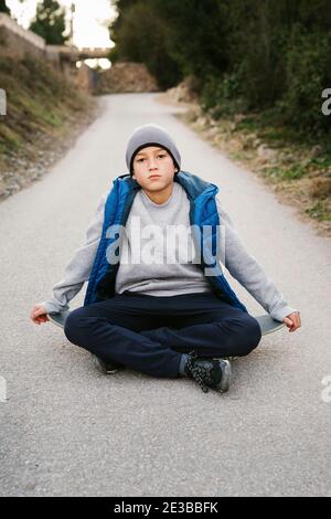 Portrait d'UN Teen Boy assis sur son skateboard une trajectoire Banque D'Images