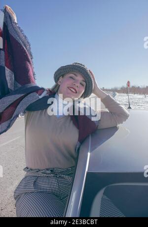 Photographie verticale d'une femme heureuse profitant de la vue enneigée sur la route d'hiver depuis sa voiture. Hiver extérieur 2021. Banque D'Images