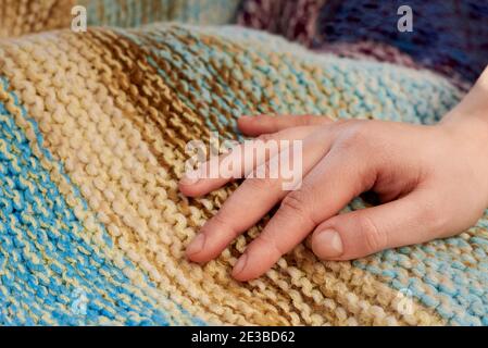 La main de la femme repose sur un tissu écossais en laine multicolore, un gros plan et un arrière-plan créatif. Banque D'Images