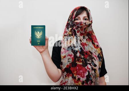 La jeune femme musulmane arabe en vêtements hijab tient le passeport de la République d'Indonésie sur fond de mur blanc, portrait de studio. Banque D'Images