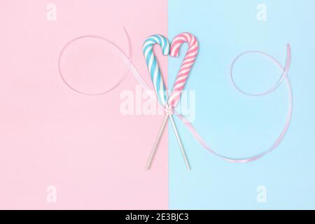 Deux Cannes en forme de coeur avec ruban en satin sur papier bleu pastel et rose. Sweet Love concept minimaliste. Historique de la Saint-Valentin Banque D'Images