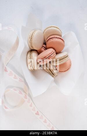 Les macarons vanille et rose sont dans un bol de coeur, fond blanc, ruban de coeur, Banque D'Images