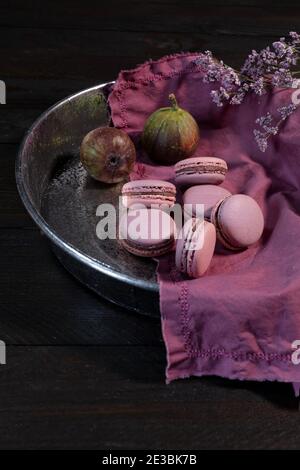 Les macarons figuiers se trouvent dans un bol en métal rond, décoré de fleurs et de figues sur une table en bois marron Banque D'Images