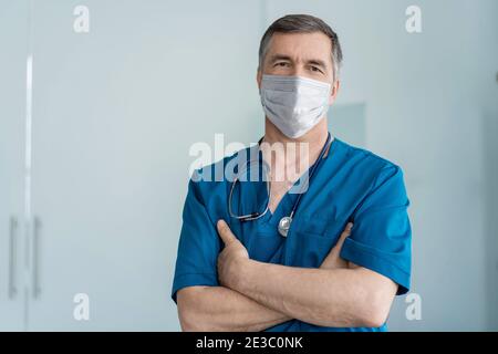 Joyeux médecin mature dans le masque facial debout à l'hôpital, les soins de santé et la médecine. Banque D'Images