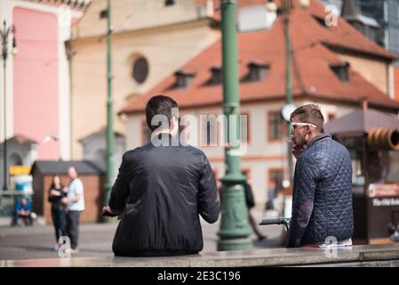 Prague, République tchèque. 09-23-2019. Deux amis du courrier, dont un fumeur, parlent et apprécient pendant une journée ensoleillée dans le centre-ville de Prague. Banque D'Images