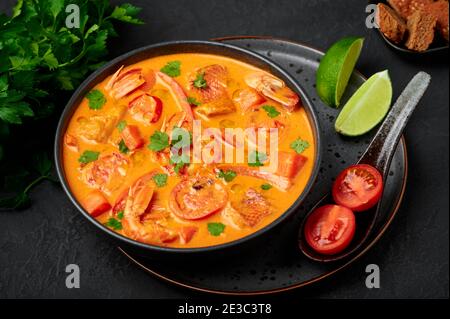 Moqueca avec poisson et crevettes dans un bol noir sur table en ardoise sombre. Plat brésilien de curry de fruits de mer avec lait de coco et légumes. Banque D'Images