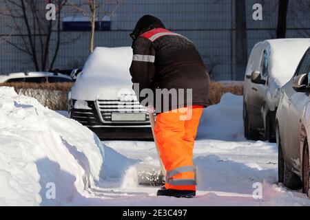 Déneigement en ville d'hiver, nettoyage des rues. Ouvrier en uniforme avec une pelle sur le parking Banque D'Images