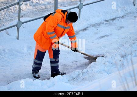 Déneigement en ville d'hiver, nettoyage des rues. Un travailleur des services communautaires en uniforme avec une pelle élimine la neige sur un trottoir Banque D'Images
