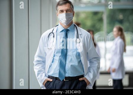 Joyeux médecin mature dans le masque facial posant à l'appareil photo, les soins de santé et la médecine. Banque D'Images