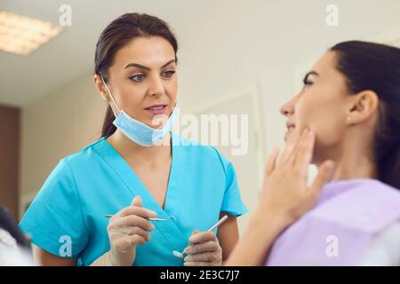 Dentiste regardant une patiente montrant une douleur dentaire et touchant la joue en clinique dentaire Banque D'Images