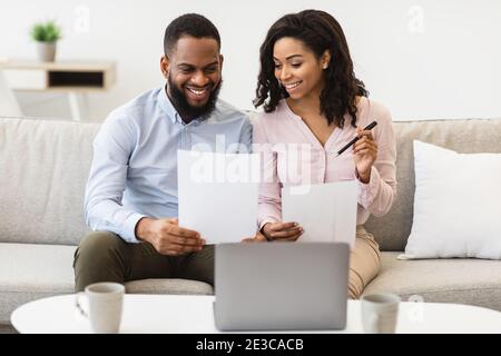 Couple noir joyeux lisant des documents à la maison, vérifiant des factures Banque D'Images