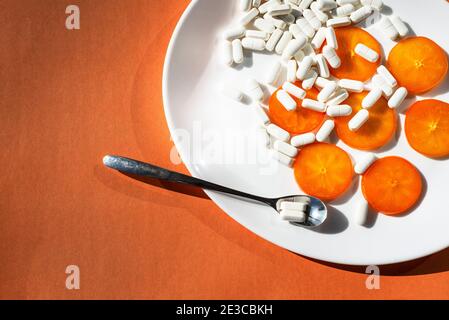 Sur une assiette ovale blanche - tranches d'orange de persimmon, capsules de suppléments minéraux et une cuillère avec une pilule. Orange. Biohaking sur des sujets de santé. Banque D'Images