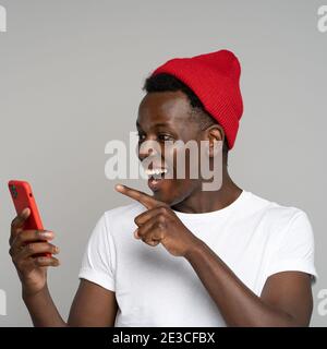 Surpris Africain hipster homme parlant dans chat vidéo pointant le doigt sur l'écran téléphone mobile, isolé Banque D'Images