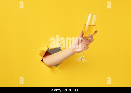 Belle main de femme avec flûte à champagne se brise à travers le fond jaune Banque D'Images