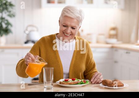 Belle vieille dame verser du jus, déjeuner dans la cuisine Banque D'Images