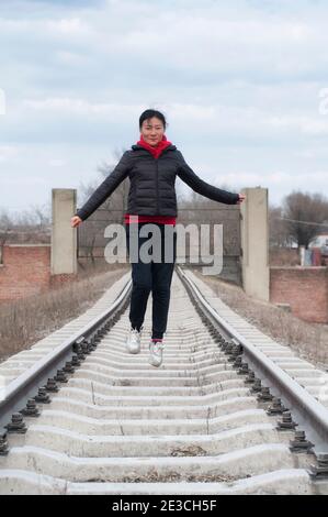 Une femme portant une veste noire et un pull à capuche rouge Sur les voies ferrées dans la ville de Zhaodong Chine dans Province de Heilongjiang sur un froid couvert da Banque D'Images