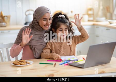 Mère musulmane et petite fille effectuant un appel vidéo sur ordinateur portable dans la cuisine Banque D'Images