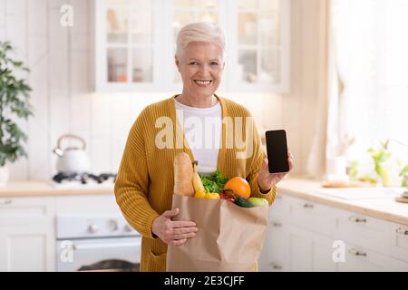 Femme aîée gaie avec sac de shopping montrant un smartphone Banque D'Images