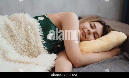 Belle jeune fille dans une nuit verte dort sur un coussin jaune sur un canapé sous une couverture blanche Banque D'Images