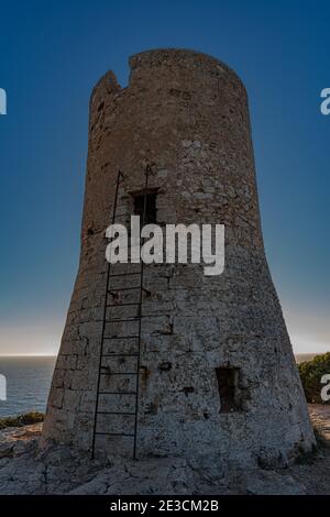 Image de la tour de guet du Cap blanc à Majorque avec le phare en arrière-plan au coucher du soleil.cette tour construite dans le s. XVI a mis en garde contre les attaques de pirates. Banque D'Images