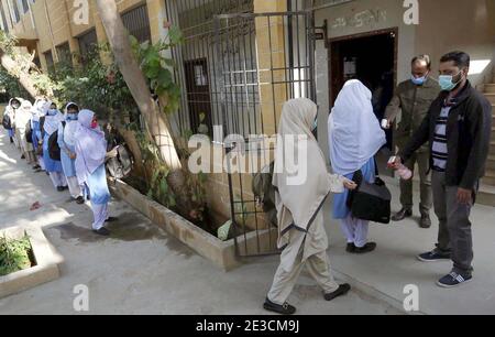 Les responsables des écoles vérifient la température corporelle des élèves et désinfectent leurs mains à l'entrée comme mesure préventive contre la propagation du coronavirus (COVID-19), tandis qu'un grand nombre d'élèves arrivent à l'école après la réouverture de l'école à Karachi le lundi 18 janvier 2021. Les écoles, les collèges, les universités et les madrasahs à travers le Pakistan ont été rouverts après la fermeture en raison de la deuxième vague de pandémie de Covid-19. Banque D'Images
