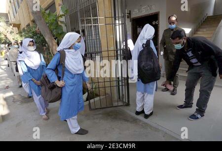 Les responsables des écoles vérifient la température corporelle des élèves et désinfectent leurs mains à l'entrée comme mesure préventive contre la propagation du coronavirus (COVID-19), tandis qu'un grand nombre d'élèves arrivent à l'école après la réouverture de l'école à Karachi le lundi 18 janvier 2021. Les écoles, les collèges, les universités et les madrasahs à travers le Pakistan ont été rouverts après la fermeture en raison de la deuxième vague de pandémie de Covid-19. Banque D'Images