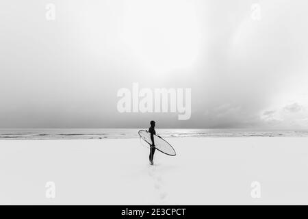 Hiver et surf avec planche de surf. Plage enneigée et surf en combinaison. Banque D'Images