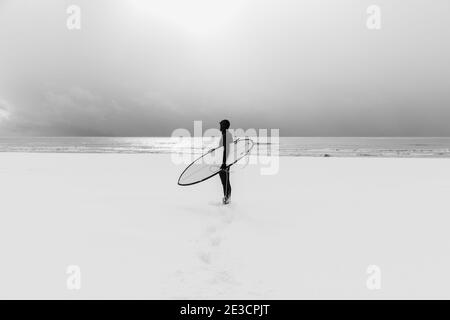 Hiver et surf avec planche de surf. Plage enneigée et surf en combinaison. Banque D'Images