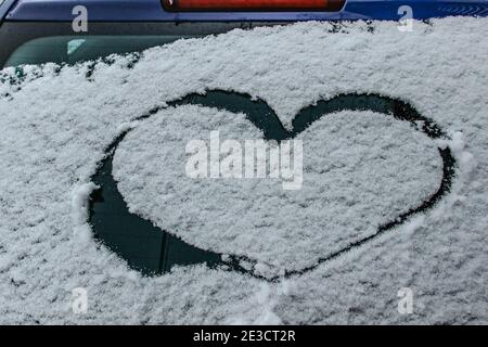 Forme de coeur sur la fenêtre de voiture enneigée. Fond d'hiver romantique.coeur dessiné à la main dans la neige fraîche.Joyeux Noël ou concept de la Saint-Valentin. Copier l'espace Banque D'Images