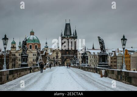 Prague, République tchèque - 14 janvier 2021. Pont Charles, tour du pont de la vieille ville recouverte de neige. Les gens qui marchent dans la ville en hiver froid Banque D'Images