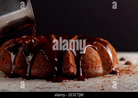 Le pudding au chocolat chaud fondu est versé d'un pichet en métal sur un gâteau au chocolat comme glaçage. Il s'écoule vers le bas et donne une flaque brune Banque D'Images