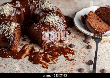 Vue latérale inclinée d'un gâteau au chocolat rond gastronomique avec des noix de coco râlées sur la glace. Deux tranches ont été retirées et placées sur une plaque en porcelaine blanche avec un moi Banque D'Images
