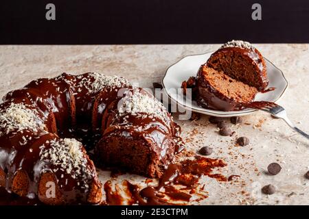 Vue latérale inclinée d'un gâteau au chocolat rond gastronomique avec des noix de coco râlées sur la glace. Deux tranches ont été retirées et placées sur une plaque en porcelaine blanche avec un moi Banque D'Images